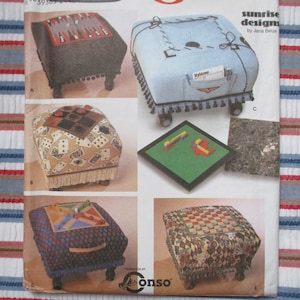 May include: Five different designs for a game-themed ottoman. The ottomans are covered in fabric with various game-themed patterns, including checkers, cards, and backgammon. The ottomans have fringe trim and wooden legs.