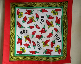Puede incluir: Bandana roja con un centro blanco con un patrón repetido de chiles rojos y la palabra "HOT" en negro. El borde es un patrón geométrico amarillo, verde y negro.