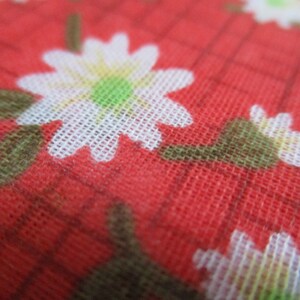 K&ouml;nnte beinhalten: Roter Stoff mit einem wei&szlig;en Blumenmuster. Die Blumen sind klein und haben ein schlichtes Design. Der Stoff hat eine gewebte Textur.