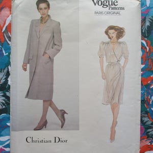 May include: Vogue Patterns Paris Original sewing pattern featuring two Christian Dior designs. One design is a long, light-colored coat with a notched collar and pockets. The other is a wrap dress with short sleeves. The background is a floral fabric.