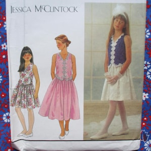 May include: A vintage sewing pattern by Jessica McClintock featuring illustrations of girls' dresses. The pattern includes a floral print dress, a pink dress, and a blue vest with a white skirt. The background is a blue floral fabric.