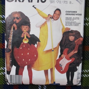 May include: A vintage sewing pattern featuring children in fruit and musical instrument costumes. The costumes include a banana, strawberry, and a guitar. The pattern's text reads "COSTUMES DEGUISEZ-VOUS" and "FUNKY FRUIT".