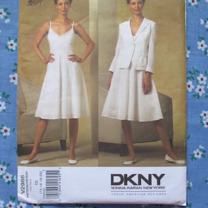 May include: A sewing pattern featuring two images of a woman in a white dress and suit. The pattern is labeled "DKNY DONNA KARAN NEW YORK VOGUE AMERICAN DESIGNER" and includes the pattern number V2966. The background is a light tan color.