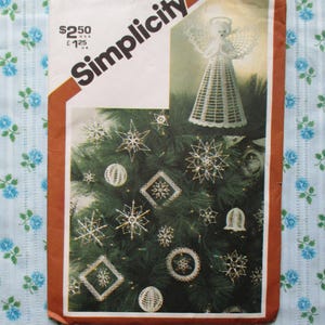 Könnte beinhalten: Simplicity-Schnittmuster mit einem Weihnachtsbaum, der mit weißen, sternförmigen Ornamenten und einem weißen Engel geschmückt ist. Das Muster befindet sich vor einem blauen Blumenmuster.