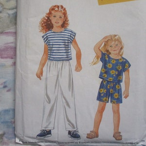 May include: A sewing pattern for two children's outfits. The first outfit is a striped blue and white top with white trousers. The second outfit is a blue top with a yellow sunflower print and matching shorts.