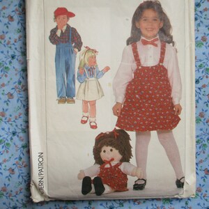 May include: A sewing pattern for children's clothing. The pattern includes instructions for making a red and white gingham dress with straps, a plaid shirt with dungarees, and a white dress with a bow. The pattern is called "Pattern/Patron".