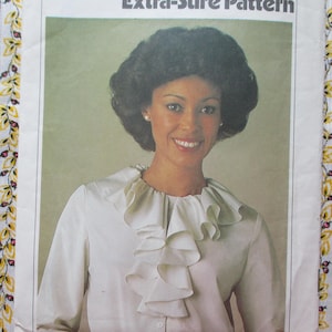 May include: A white blouse with a large ruffled collar. The model is wearing the blouse and has dark hair and brown eyes.