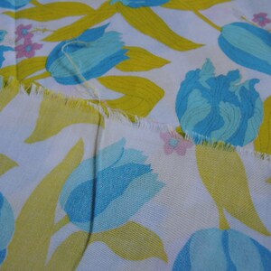 May include: White fabric with a repeating pattern of blue and yellow tulips. The fabric has a frayed edge.