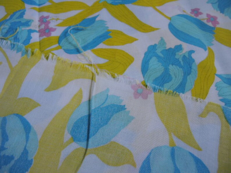 May include: White fabric with a repeating pattern of blue and yellow tulips. The fabric has a frayed edge.