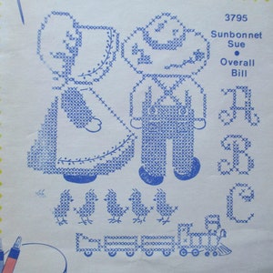 May include: A cross-stitch pattern featuring two children, a girl in a sunbonnet and a boy in overalls, with the text "Sunbonnet Sue" and "Overall Bill". The pattern also includes a train and birds.