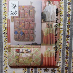 May include: A sewing pattern booklet with the title "Compliments of Butterick Patterns". The booklet features illustrations of a pink and white table cloth, a pink table cloth with lace trim, and a pink and white hanging organizer with 12 pockets.