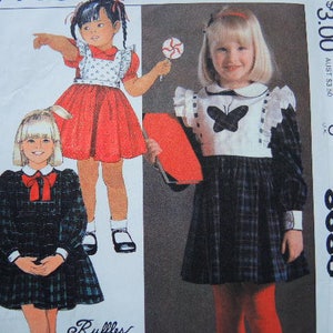 May include: A sewing pattern for two children's dresses. The pattern is for a plaid dress with a white collar and a red dress with a white bib. The pattern number is 8680 and the price is $3.00.