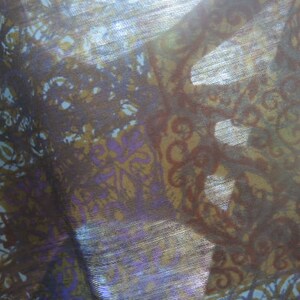May include: A close-up of a sheer fabric with a brown, purple, and blue floral pattern. The fabric is translucent and has a subtle shimmer.