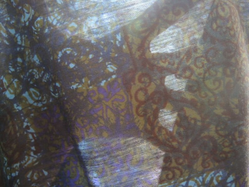 May include: A close-up of a sheer fabric with a brown, purple, and blue floral pattern. The fabric is translucent and has a subtle shimmer.