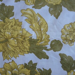 May include: A white fabric with a repeating pattern of yellow flowers and green leaves. The flowers have a detailed design and are arranged in a symmetrical pattern.