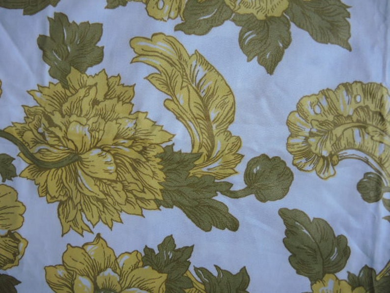 May include: A white fabric with a repeating pattern of yellow flowers and green leaves. The flowers have a detailed design and are arranged in a symmetrical pattern.