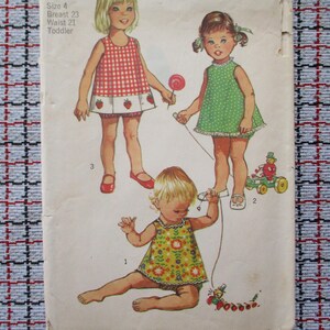 Könnte beinhalten: Vintage Schnittmuster für Kleider für Kleinkinder. Die Illustration zeigt drei junge Mädchen in Kleidern mit verschiedenen Mustern. Der Text auf dem Muster gibt die Größe 4 an, mit 58 cm Brustumfang und 53 cm Taillenumfang.