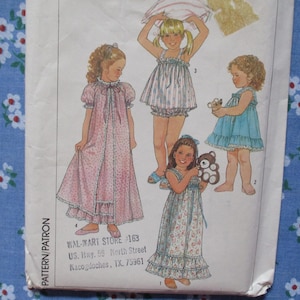 May include: A vintage sewing pattern featuring illustrations of young girls in various sleepwear styles. The designs include a long pink robe, a striped top and shorts set, a blue dress, and a floral nightgown. The pattern is from Wal-Mart Store 163.