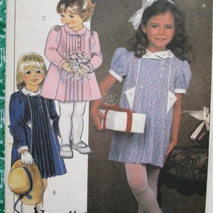 Puede incluir: Patrón de costura de vestido infantil vintage con ilustraciones de niñas con vestidos. Los vestidos son en azul, rosa y marino, con detalles blancos. El patrón incluye un lazo blanco y una caja de regalo.