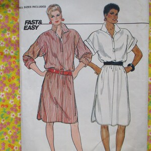 Op de afbeelding: Een naaipatroon met twee vrouwen die verschillende stijlen jurken dragen. De jurk aan de linkerkant is een gestreepte shirtjurk met een knoopsluiting en een riem. De jurk aan de rechterkant is een witte jurk met een knoopsluiting en een riem. Het patroon is gemarkeerd met "Fast & Easy" en bevat alle maten.