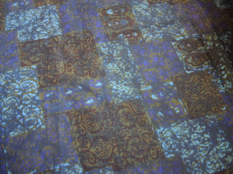 May include: A fabric with a patchwork design featuring various shades of blue, brown, and purple. The fabric has a repeating pattern of intricate floral designs.