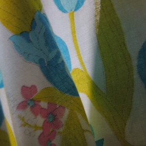 May include: White fabric with a floral pattern featuring blue, yellow, and pink flowers. The fabric has a subtle sheen and a soft texture.