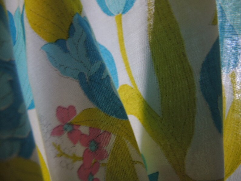 May include: White fabric with a floral pattern featuring blue, yellow, and pink flowers. The fabric has a subtle sheen and a soft texture.