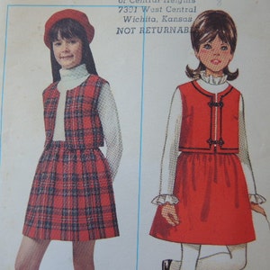 May include: Vintage sewing pattern featuring two girls' outfits. One outfit includes a red plaid skirt, vest, and beret, paired with a white turtleneck. The other outfit is a red dress with a white blouse and decorative buttons. The text on the pattern reads "7301 West Central Wichita, Kansas NOT RETURNABLE."
