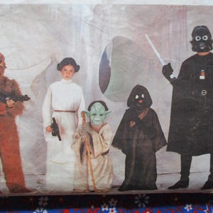 May include: A vintage sewing pattern featuring Star Wars character costumes. The costumes include Chewbacca, Princess Leia, Yoda, a Jawa, and Darth Vader. The pattern shows the characters in full costume, with weapons and accessories.