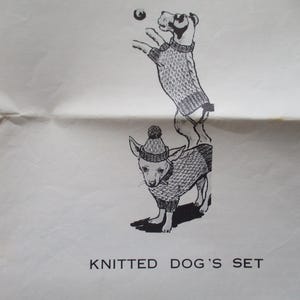 May include: Black and white illustration of two dogs wearing knitted sweaters and a hat. One dog is standing on its hind legs, reaching for a ball. The other dog is standing on all fours. The text "KNITTED DOG'S SET" is below the dogs.