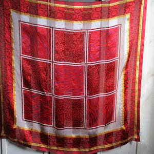 May include: A red and gold patterned silk scarf with a white centre featuring a grid of nine squares. Each square has a different red and gold pattern.