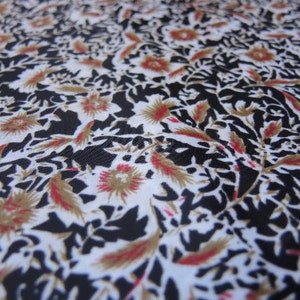 May include: White fabric with a black and brown floral pattern. The pattern features stylised leaves and flowers with red accents.