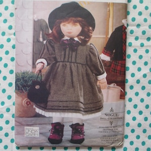 May include: A doll wearing a gray dress, black hat, and burgundy boots, holding a black purse. The doll is featured on a Vogue Doll Collection pattern. The pattern includes the text "FULL-COLOR IRON ON TRANSFER FOR THE FACE IS INCLUDED".