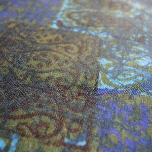 May include: A close-up of a fabric with a swirling pattern in shades of blue, green, and brown. The fabric has a textured surface and a subtle sheen.