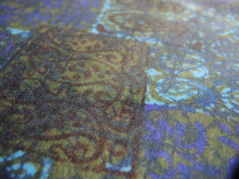 May include: A close-up of a fabric with a swirling pattern in shades of blue, green, and brown. The fabric has a textured surface and a subtle sheen.