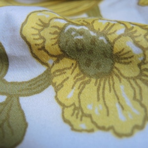 May include: A white fabric with a yellow floral pattern. The flowers are stylized and have a textured appearance.