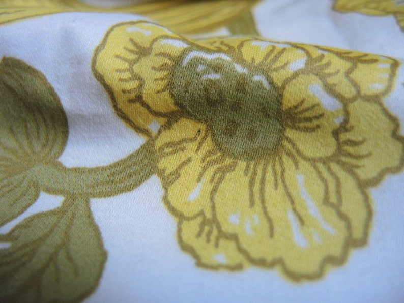May include: A white fabric with a yellow floral pattern. The flowers are stylized and have a textured appearance.
