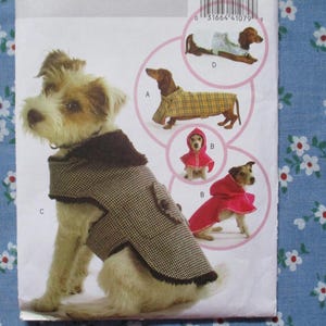 May include: A dog wearing a brown and black patterned coat with a dark brown collar. The image also shows illustrations of dogs in various outfits, including a red hooded cape and a yellow plaid coat. The background is a light blue floral pattern.