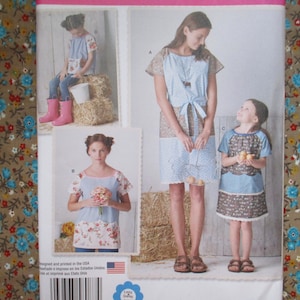 May include: A sewing pattern for three different dresses. The dresses are all blue and white with floral patterns. The pattern includes instructions for making the dresses in sizes for children.