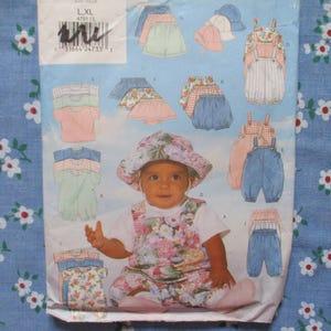Puede incluir: Un patrón de costura vintage para ropa de bebé con ilustraciones de petos, pantalones cortos y sombreros. El patrón incluye una foto de un bebé con un conjunto y sombrero con estampado floral. El fondo es una tela floral azul.