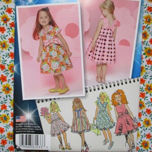 May include: A sewing pattern booklet with a photo of a girl wearing a floral dress and another girl wearing a pink polka dot dress. The booklet also includes illustrations of four girls wearing different dresses.