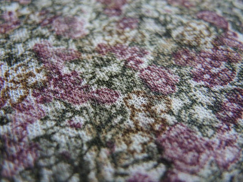 May include: Close-up of a fabric with a floral pattern. The fabric is white with brown, pink, and green flowers.
