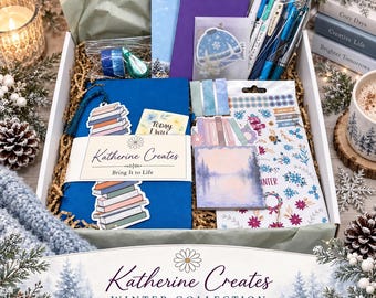 May include: A stationery gift box containing a blue journal with a Katherine Creates band, a purple notebook, blue and teal pens, washi tape, a winter-themed sticker sheet, a landscape notepad, and a small card reading Today I Will.