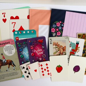 May include: A collection of assorted playing cards and stationery items including a card with a horse illustration labeled Deutsches Reitpferd, Fashion Show cards, a card with a strawberry, a plum, a fairy illustration, and various numbered playing cards.