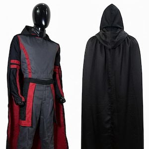 May include: A costume set featuring a grey top and pants with red accents, paired with a black hooded cape. The outfit includes a long-sleeved shirt with red stripes on the sleeves, matching grey trousers, and a solid black cape with a hood.