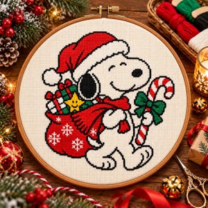 May include: A circular wooden embroidery hoop containing a cross-stitch pattern of a white beagle wearing a red Santa hat and scarf. The character carries a red sack filled with gifts and a yellow star, while holding a red and white candy cane.