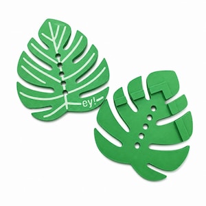 Könnte beinhalten: Zwei grüne blattförmige Objekte mit Ausschnitten. Das linke Objekt zeigt weiße Blattadern und den in Weiß gedruckten Text "ey!". Das rechte Objekt weist eine Reihe kreisförmiger Löcher entlang der Mittelrippe sowie erhabene rechteckige Strukturen auf der Oberfläche auf.