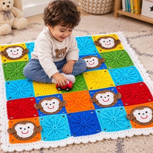 Op de afbeelding: Een vierkante gehaakte babydeken met een raster van kleurrijke vierkanten in rood, oranje, geel, groen en blauw. Verschillende vierkanten tonen een applicatie van een wit en bruin apengezicht met een glimlach. De deken heeft een witte schulprand.