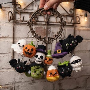 May include: A collection of small, crocheted Halloween-themed keychains hanging from a circular metal ring. The figures include a white ghost, orange pumpkin, skull with a top hat, green monster, black bat, purple witch hat, candy corn, and mummy.