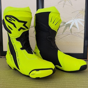 Puede incluir: Un par de botas de motocicleta en color amarillo neón y negro con el logotipo de Alpinestars en la espinillera y el deslizador de la puntera. Las botas tienen un diseño de corte alto con paneles de ventilación de malla negra y refuerzos.